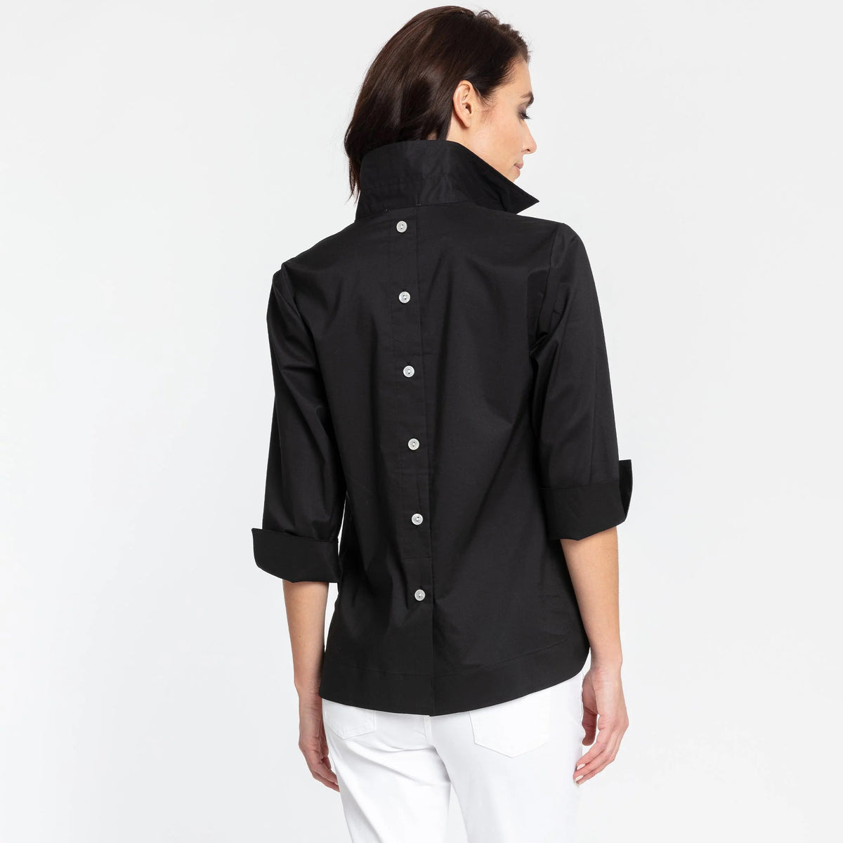 A person with short, dark hair is standing against a plain background, wearing the HINSON WU - AILEEN 3/4 SLEEVE TOP in black with a shirt collar and the sleeves rolled up, paired with white pants. The top features three buttons at the neckline. The individual is looking directly at the camera and smiling slightly.