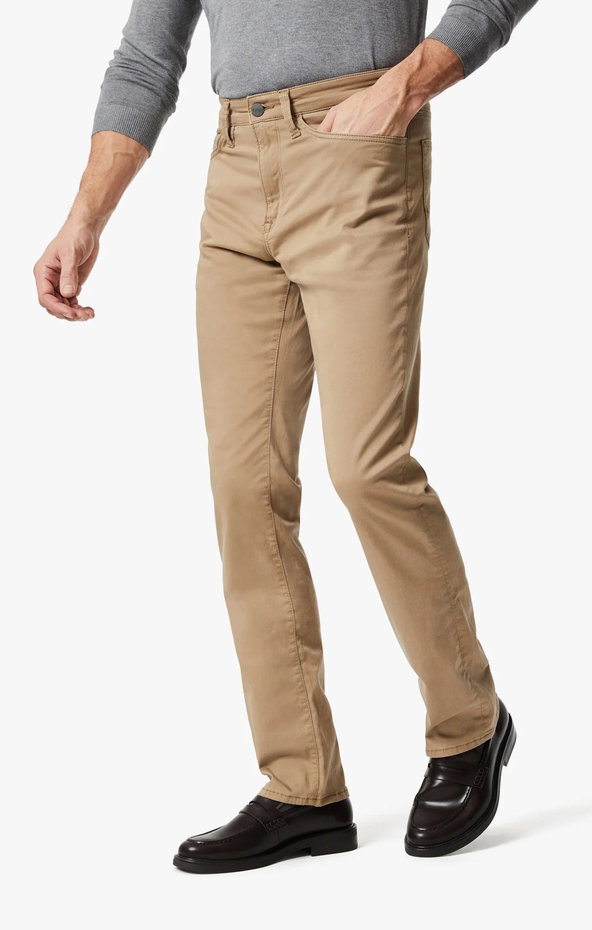 A man walks confidently in a light gray long-sleeve sweater, 34 HERITAGE - CHARISMA RELAXED STRAIGHT PANTS IN KHAKI TWILL by 34 HERITAGE, and dark brown shoes against a plain white background.