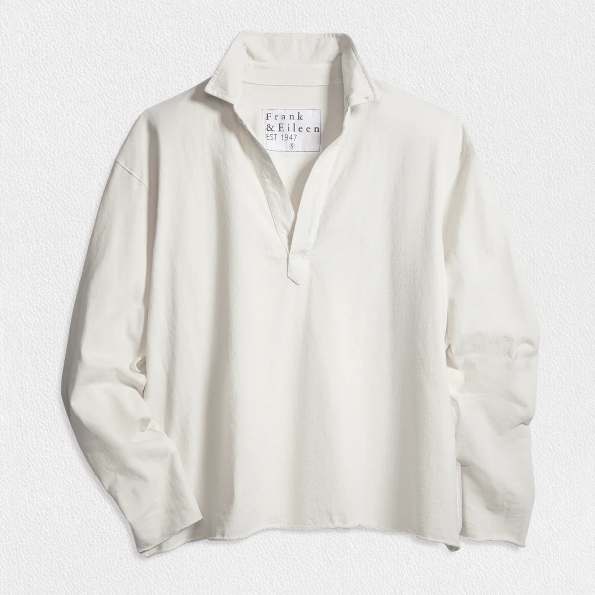 The FRANK &amp; EILEEN Patrick Popover Henley in Heritage Jersey White, a relaxed-fit long-sleeve shirt with an open neckline, is shown laid flat on a textured white surface. The tag displays the FRANK &amp; EILEEN brand name.