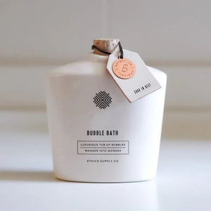 The ETHICS SUPPLY CO - SOAK IN REST CERAMIC BUBBLE BATH features a white bottle with a cork stopper and a tag. It reads "Luxurious Tub of Bubbles" and "Wander Into Wonder," offering an enchanting bathing experience with the soothing aroma of pink jasmine.