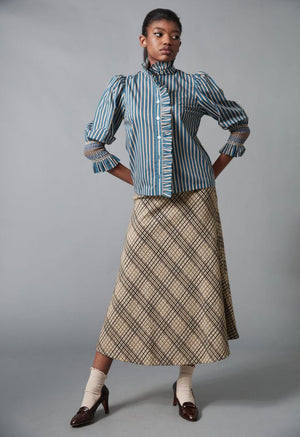 A woman models the HOPE FOR FLOWERS - FRILLED BUTTON DOWN SHIRT by HOPE FOR FLOWERS, made from GOTS certified organic cotton, with a high collar and wide sleeves, paired with flared blue jeans featuring fringe along the side seams.