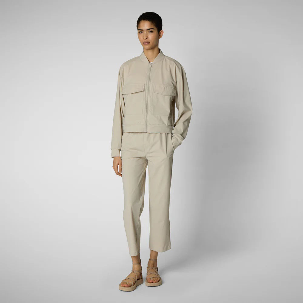 A person with shoulder-length hair and a neutral expression wears a white long-sleeve shirt, SAVE THE DUCK MILAN PULL ON PANT in black wrinkle-free fabric, and black slip-on shoes. Their hands rest at their sides against a plain background.