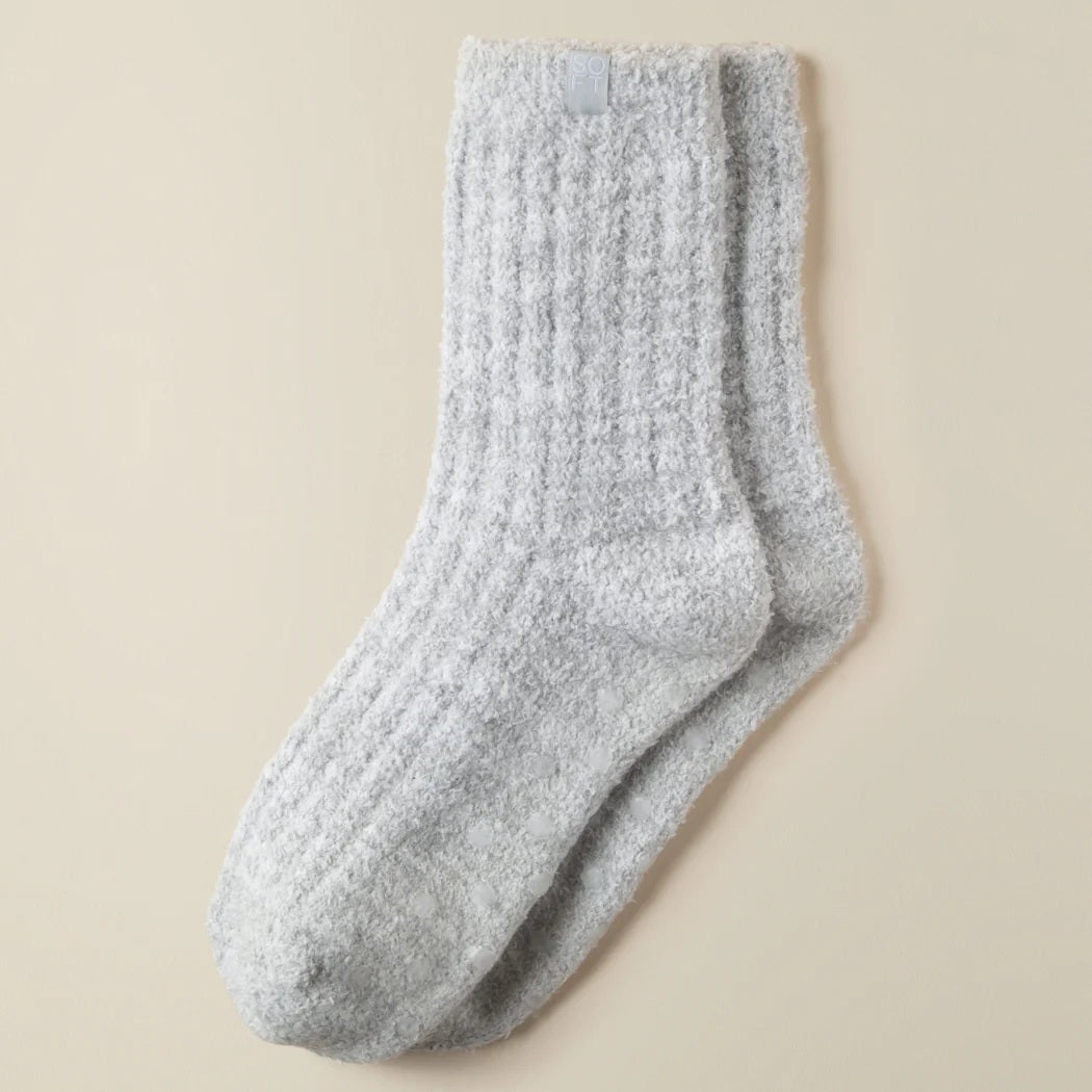 Two feet in SOFTIES - MARSHMALLOW CREW SOCKS IN HEATHER GREY are raised against a plain beige background. These ribbed, heather grey SOFTIES socks look ultra-soft and comfortable—perfect for lounging.