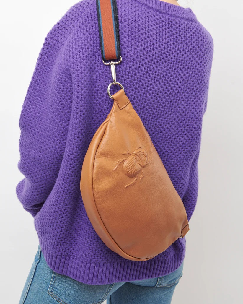 The GABRIELE FRANTZEN - SCARAB XL Leather Beltbag in Cognac features a brown Italian leather construction with an embossed scarab beetle design on the front, complemented by a black adjustable crossbody strap and silver hardware. The bag is displayed against a plain white background.