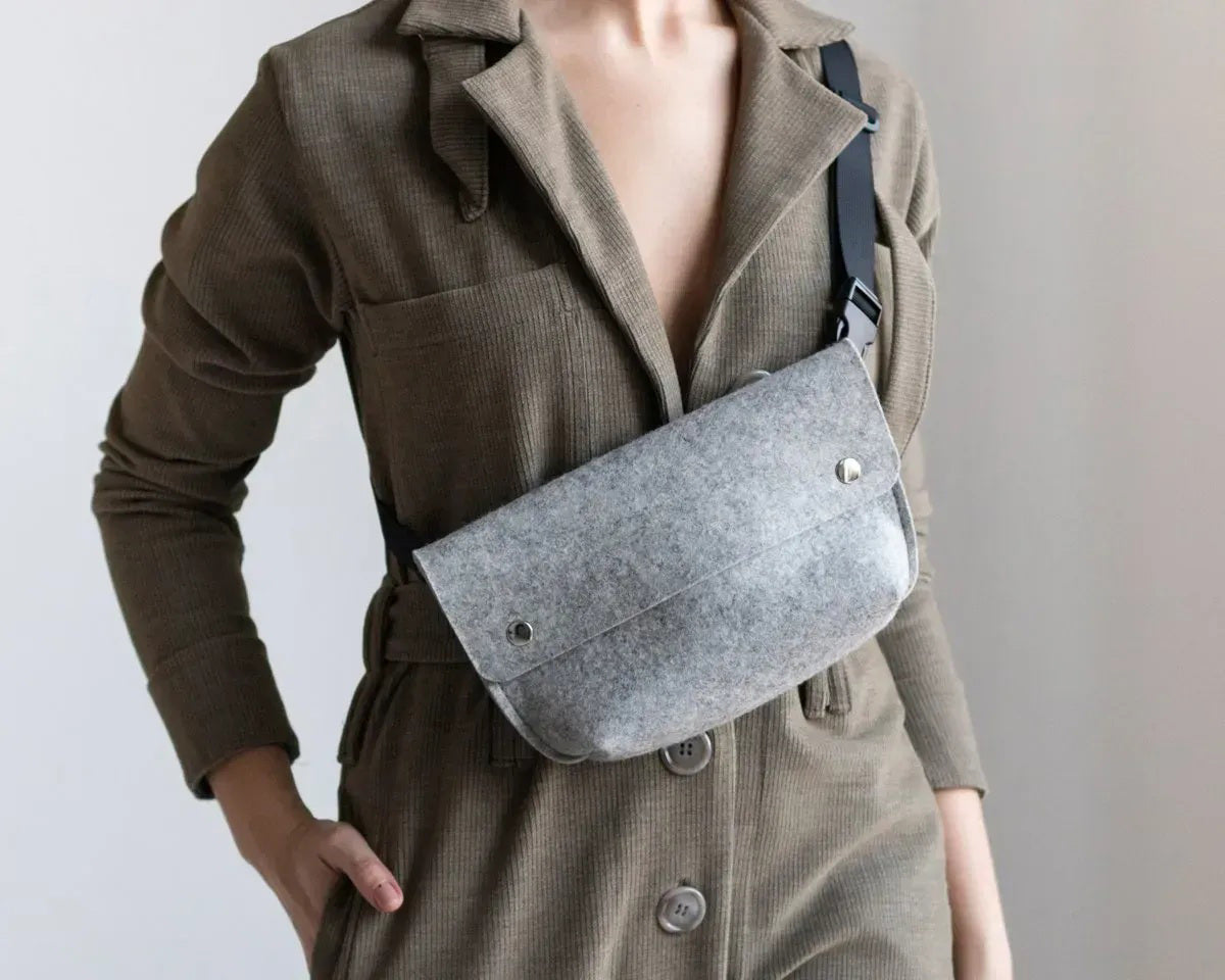 The WOOLBERRY - FELTED WOOL BELT BAG by WOOLBERRY is a small green belt bag crafted from felted wool, featuring a flap secured by two silver snap buttons, and is displayed against a white background.