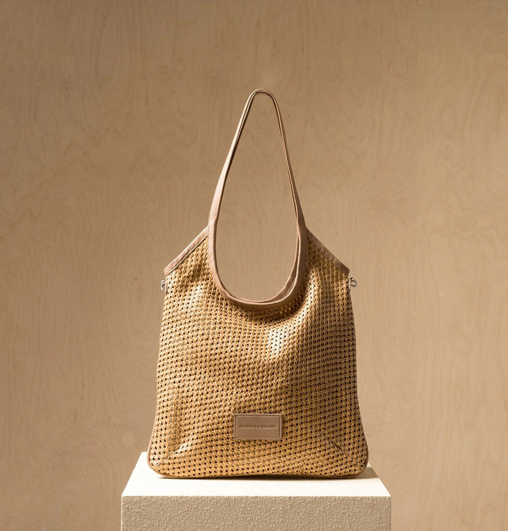 The DANIELA LEHAVI - ALBA HOBA SAC, a tan woven handbag with a single leather crossbody strap from DANIELLA LEHAVI, is displayed on a light pedestal against a beige background.