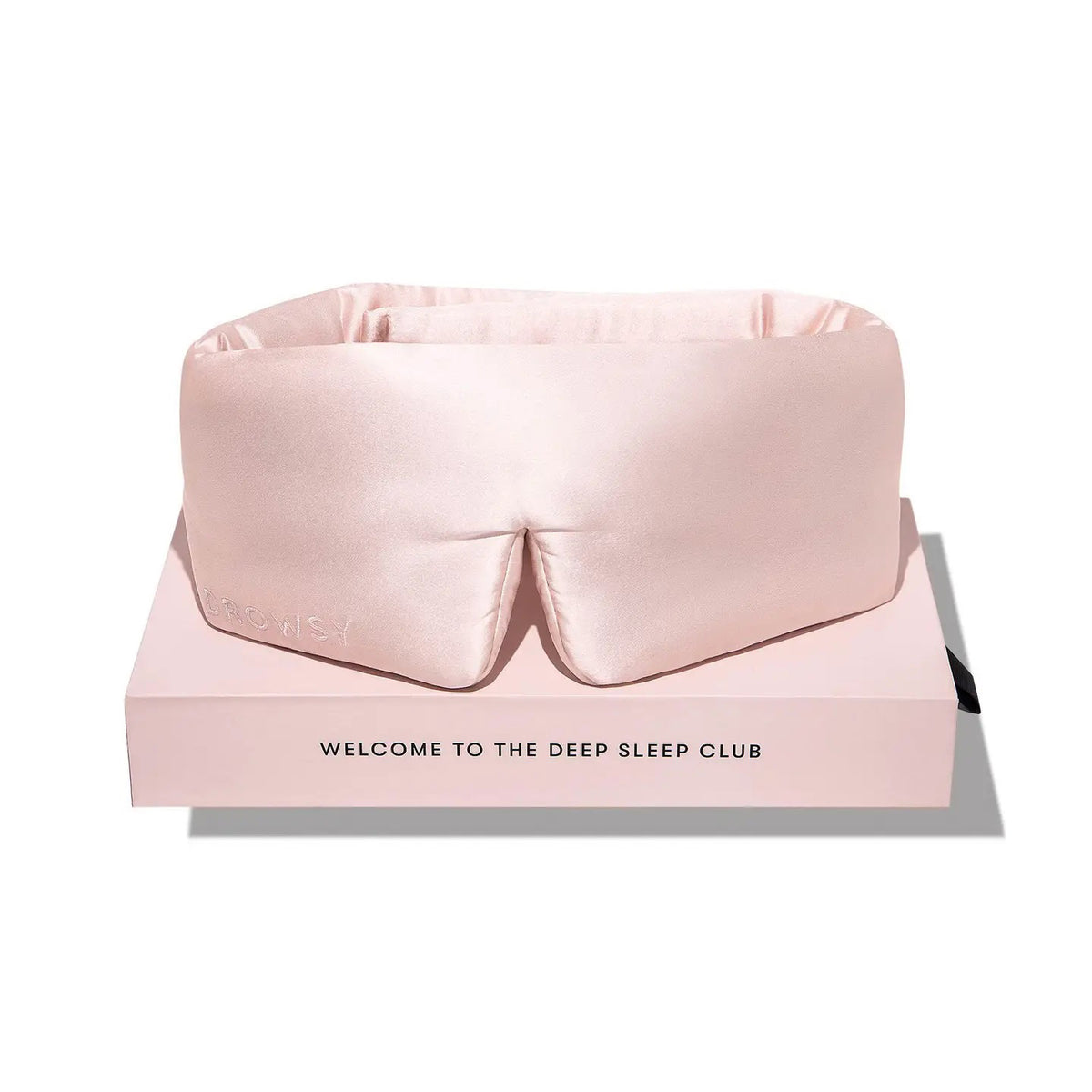 A person wearing a white tank top is lying on a pillow with the DROWSY - SATIN SLEEP MASK by DROWSY SLEEP CO covering their eyes. They look relaxed, enjoying beauty sleep as their hand rests gently on the pillow.