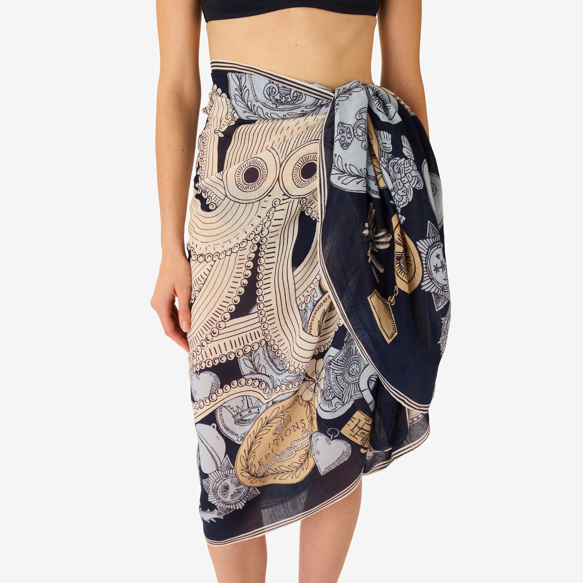 A woman, her face partially visible from the nose down, wears a sleeveless cream top and the INOUI EDITIONS - OCTOPUS SCARF IN NAVY by INOUI, featuring intricate hand-printed designs and text elegantly tied around her neck.