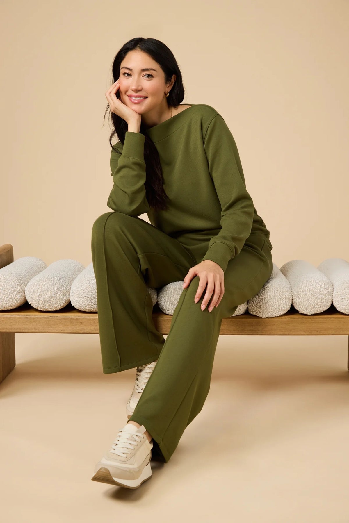 A woman wears a SOFTIES - DREAMTECH BOAT NECK WITH PINTUCK PANT SET in olive green, featuring a long-sleeve boat neck top and matching wide-leg pintuck pants.