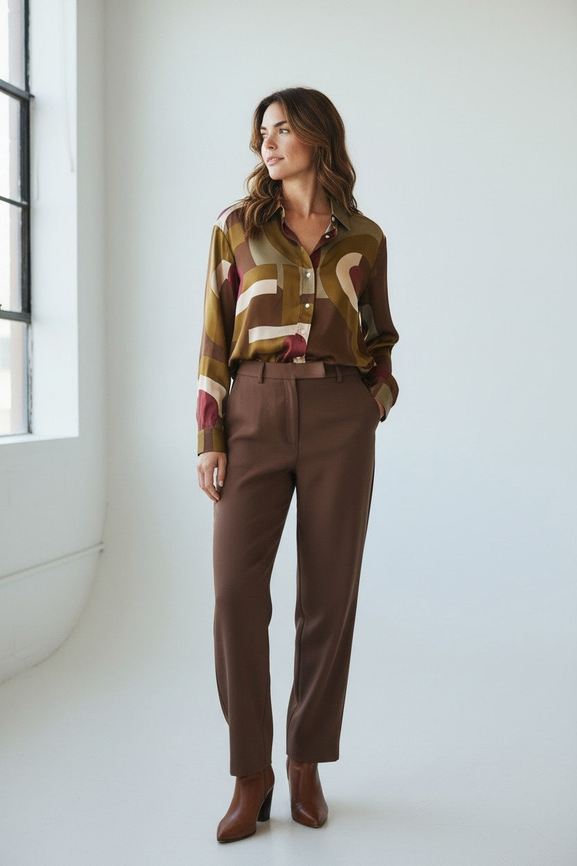 A woman with wavy brown hair wears the HARTFORD Cinema Shirt in viscose with a brown and raspberry print, looking to the side and smiling softly against a plain light background.