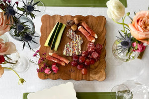The ETUHOME Natural Square Scalloped Cutting Board, Medium, crafted from durable acacia wood, stands upright against a light gray wall on a white marble surface.