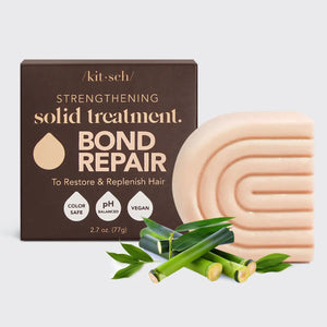 A KITSCH - STRENGTHENING BOND REPAIR SOLID HAIR MASK BAR rests by its brown box with bamboo stems, highlighting its vegan keratin formula for glass hair that's color safe and pH balanced.