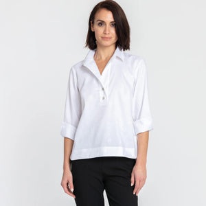 A woman with short dark hair models the HINSON WU - AILEEN 3/4 SLEEVE POLISHED COTTON SHIRT in navy, featuring a collared neckline, stretch fabric, and three buttons. She pairs it with white pants and poses against a plain light gray background.