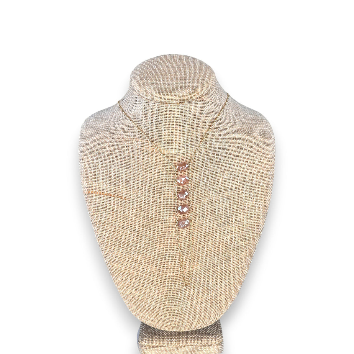 The GOLDISH - LADDERS TO BLISS PINK MOONSTONE NECKLACE features a gold vertical pendant with five pink moonstones, displayed on a beige textured bust against a white background, representing balance and harmony from GOLDISH.