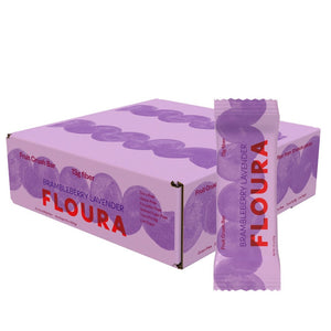 A box and a wrapped FLOURA & CO BRAMBLEBERRY LAVENDER FLOUR FIBER CRUSH BAR made with prebiotic fiber. The lavender packaging features purple/red text, large purple circles, and highlights these flavorful fiber bars.