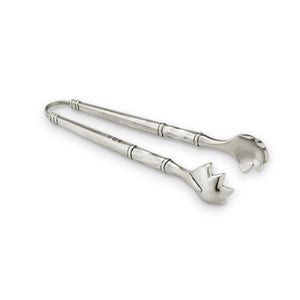 A bundle of fresh asparagus in a white rectangular dish with metal handles sits beside a folded green napkin and MATCH - PEWTER TONGS by MATCH, all displayed on a patterned gray surface.