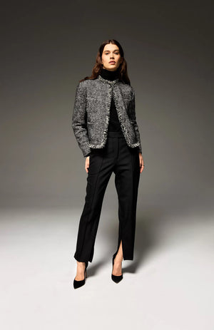 A woman stands confidently against a gradient background, wearing the SEVENTY - Wool Blend Jacket with Puffer Back by SEVENTY. She pairs the grey jacket with high collar with black tailored pants featuring a front slit and completes her outfit with black high-heeled shoes. Her long, dark hair is styled in loose waves as she looks directly at the camera.