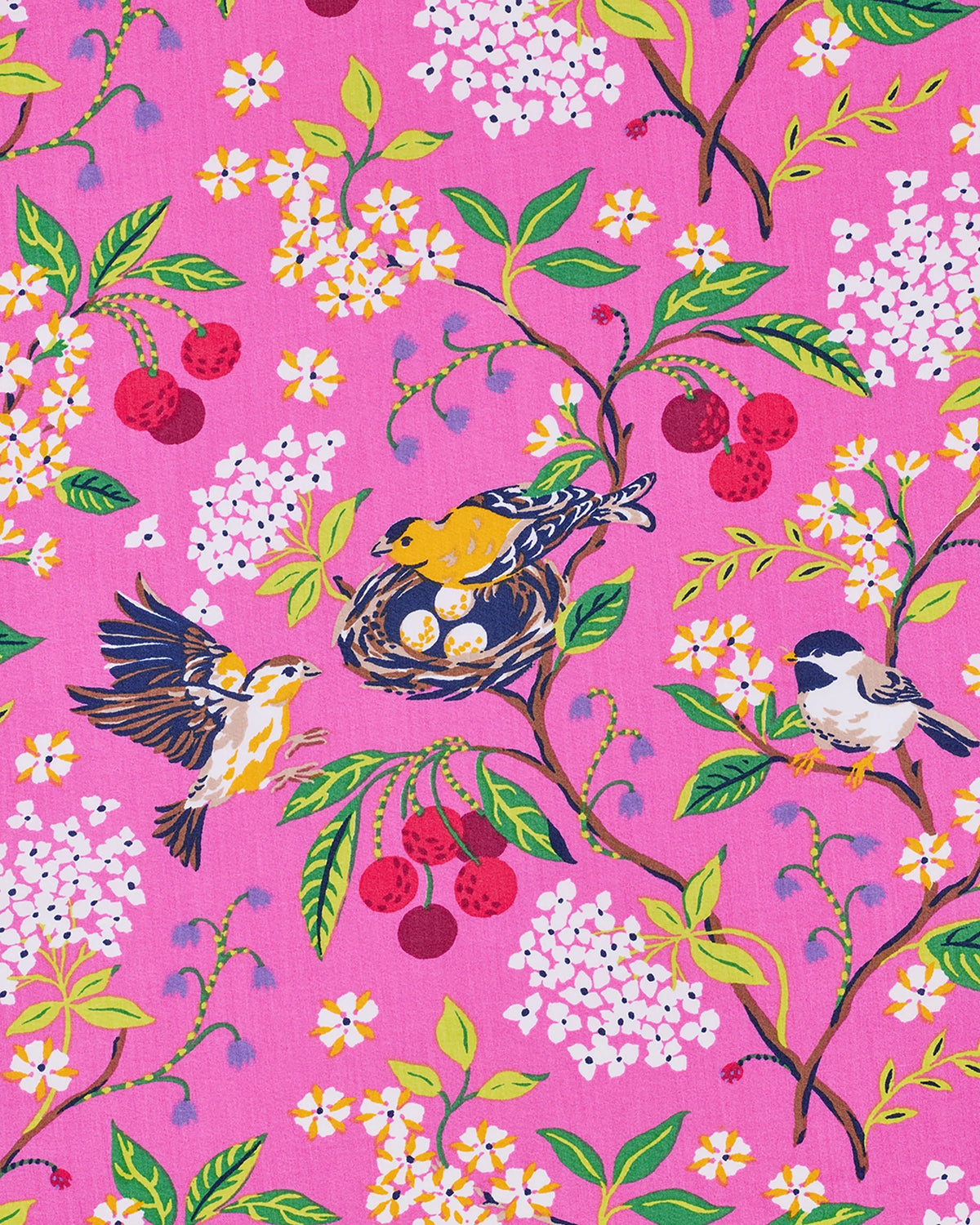 A woman wearing the PRINTFRESH Bird & Blossom Ruffle Pajama Short Set, featuring a pink, nature-inspired floral and bird print, stands against a plain light-colored wall with one hand in her shorts pocket, looking at the camera.