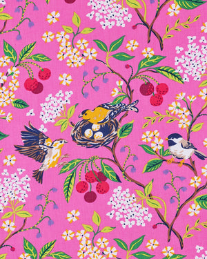 A woman wearing the PRINTFRESH Bird & Blossom Ruffle Pajama Short Set, featuring a pink, nature-inspired floral and bird print, stands against a plain light-colored wall with one hand in her shorts pocket, looking at the camera.