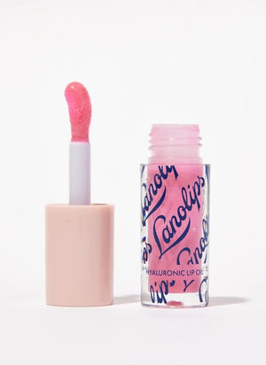 A woman with glossy pink lips holds a tube of LANOLIPS Hyaluronic Lip Oil in Raspberry near her face, looking upward with a slight smile, showcasing the non-sticky lip oil’s effortless lip hydration.