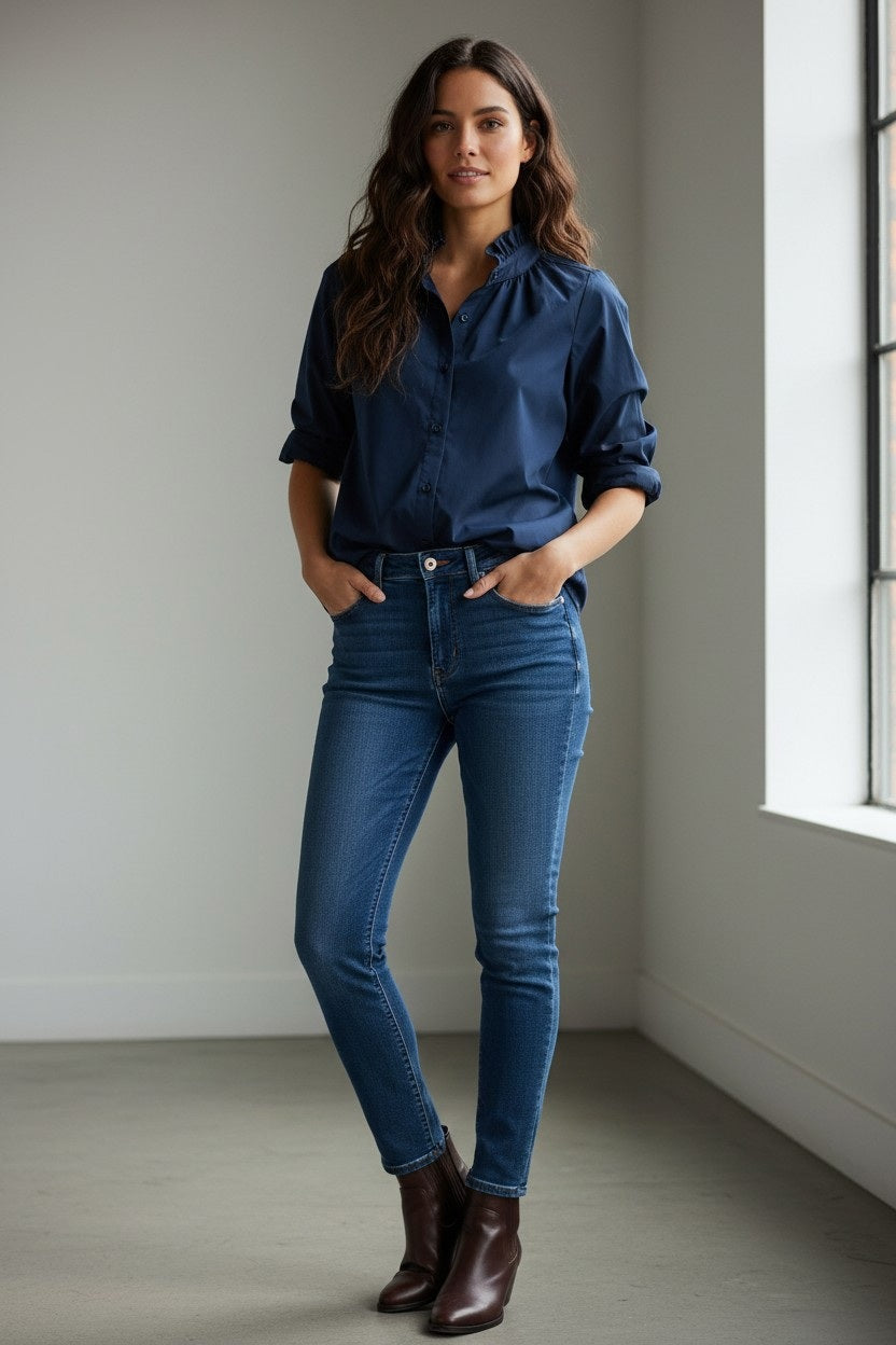A person stands outdoors with hands on hips, smiling, wearing sunglasses, a wide-brimmed hat, gold jewelry, white pants, and the KMJ SOUTHERN LOVER SHIRT IN NAVY by KMJ. The background is light and neutral.