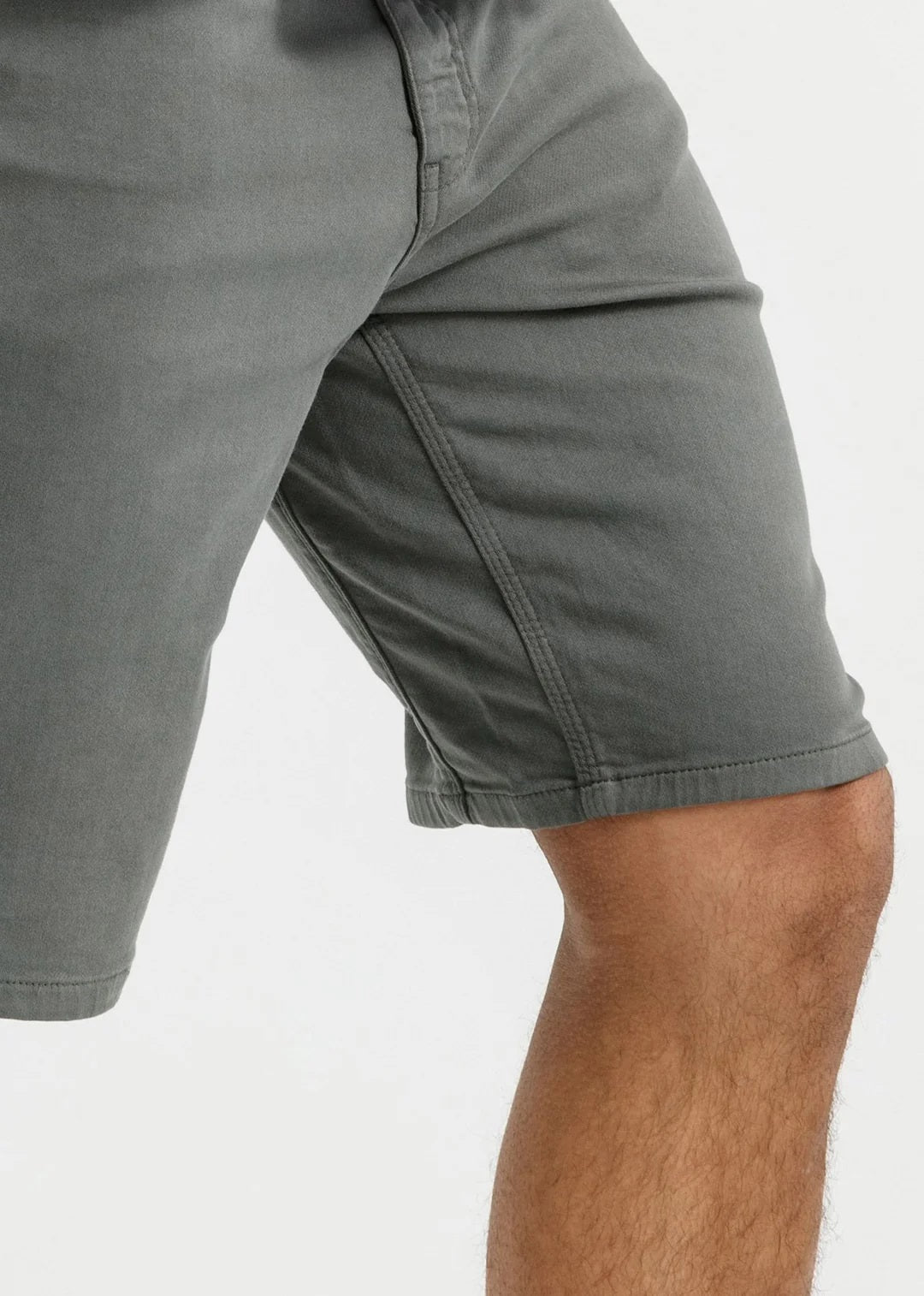 A person stands against a plain light background, wearing a white T-shirt, DUER No Sweat Relaxed Shorts in Gull made from stretch fabric, and white sneakers, with one hand in their pocket.