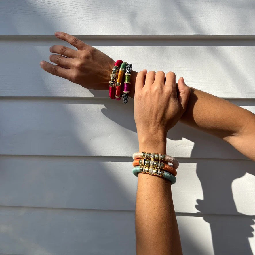 The HOLST + LEE - LUXE CLASSIC BRACELET by HOLST &amp; LEE features an elegant orange cord with gold-plated accents, including a rectangular gold clasp adorned with several gold and diamond-encrusted beads near the clasp.