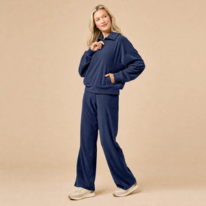 A woman seated on the floor wearing a Softies - Serenity 1/4 Zip Top with Wide Leg Pant lounge set in midnight, featuring a navy blue quarter-zip pullover and matching wide-leg lounge pants.