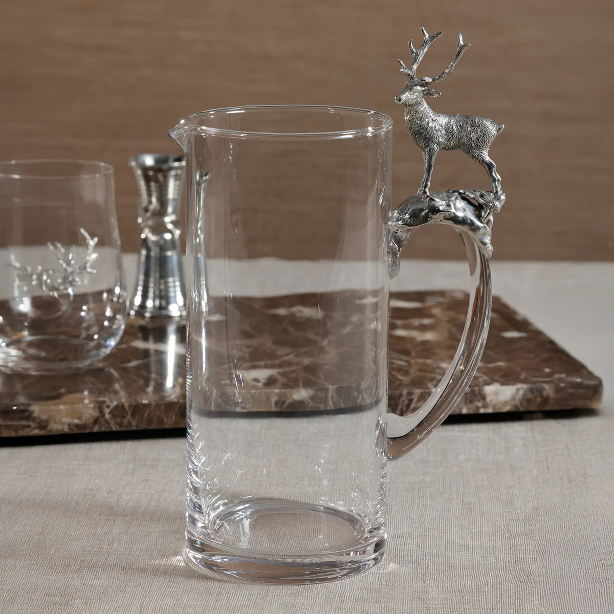 The ZODAX ST. MORITZ PEWTER PITCHER is a 1500 ml clear glass pitcher with a handle showcasing a detailed silver stag on a branch, a cylindrical shape, and a small spout—an elegant piece for any kitchen storage box collection.