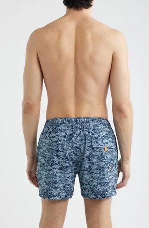 A shirtless man stands with hands in his pockets against a plain light background, modeling SAVE THE DUCK's Ademir Swim Trunks in Ondine Off White on Blue, crafted from quick-dry recycled polyester.