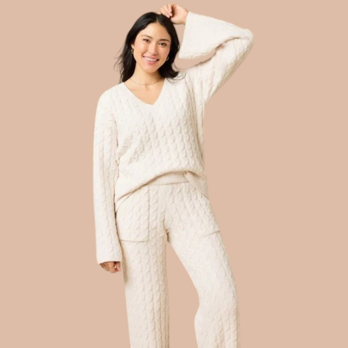 A woman wearing the SOFTIES CABLE KNIT MARSHMALLOW V-NECK WITH FLARED SLEEVE AND PANT SET, a marshmallow-soft, cream-colored cable knit v-neck sweater with wide sleeves and matching lounge pants.