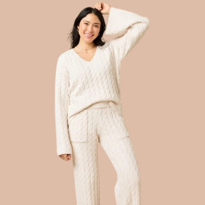 A woman wearing the SOFTIES CABLE KNIT MARSHMALLOW V-NECK WITH FLARED SLEEVE AND PANT SET, a marshmallow-soft, cream-colored cable knit v-neck sweater with wide sleeves and matching lounge pants.