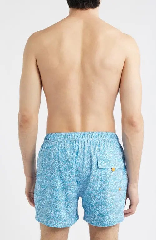 A shirtless man wears SAVE THE DUCK - ADEMIR swim trunks in light blue corals NO FISHING, made from quick-dry recycled polyester with a black drawstring, standing against a plain white background.