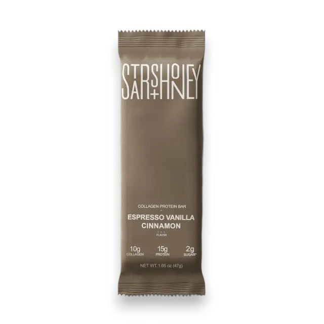 A brown STARS+HONEY - ESPRESSO VANILLA CINNAMON collagen protein bar wrapper labeled with its name and featuring nutrition details—10g collagen, 15g protein, and 2g sugar—lies on a matching brown surface, evoking classic cappuccino and espresso flavors.