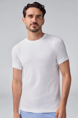 A man with short dark hair and a beard wears a slim fit white MACK WELDON - 18 HOUR JERSEY CREWNECK UNDERSHIRT and light blue pants, standing in profile against a plain light gray background.