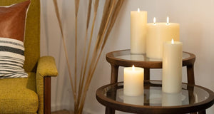 An elegant, single UYUNI - IVORY PILLAR CANDLE 3X8 by PIFFANY, with a soft, steady flame glowing at the top, stands tall against a plain white background.