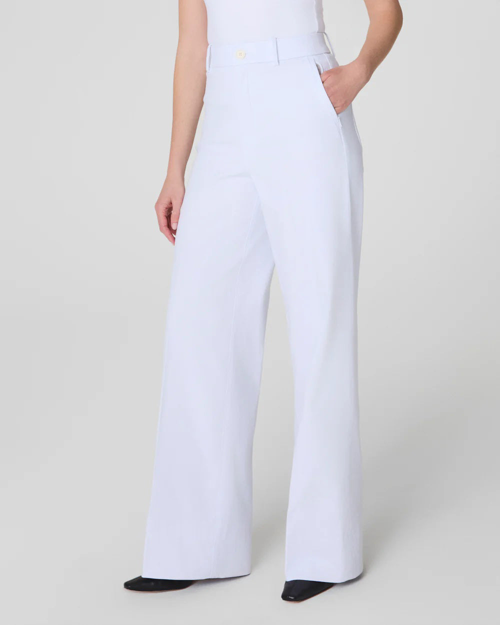 Rear view of a person modeling the SPANX - STRETCH TWILL WIDE LEG PANT in crisp white with a matching top. Their right hand rests casually at their side, complemented by sleek black pointy shoes, all set against a plain light background.