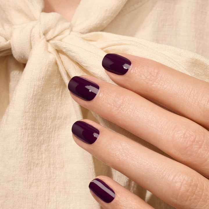 A dark maroon background features two elongated, curved white shapes—one larger, one smaller—forming an abstract, fluid design evocative of the deep, luxurious tones in MANUCURIST - GREEN™ NAIL POLISH IN EGGPLANT by MANUCURIST INC.