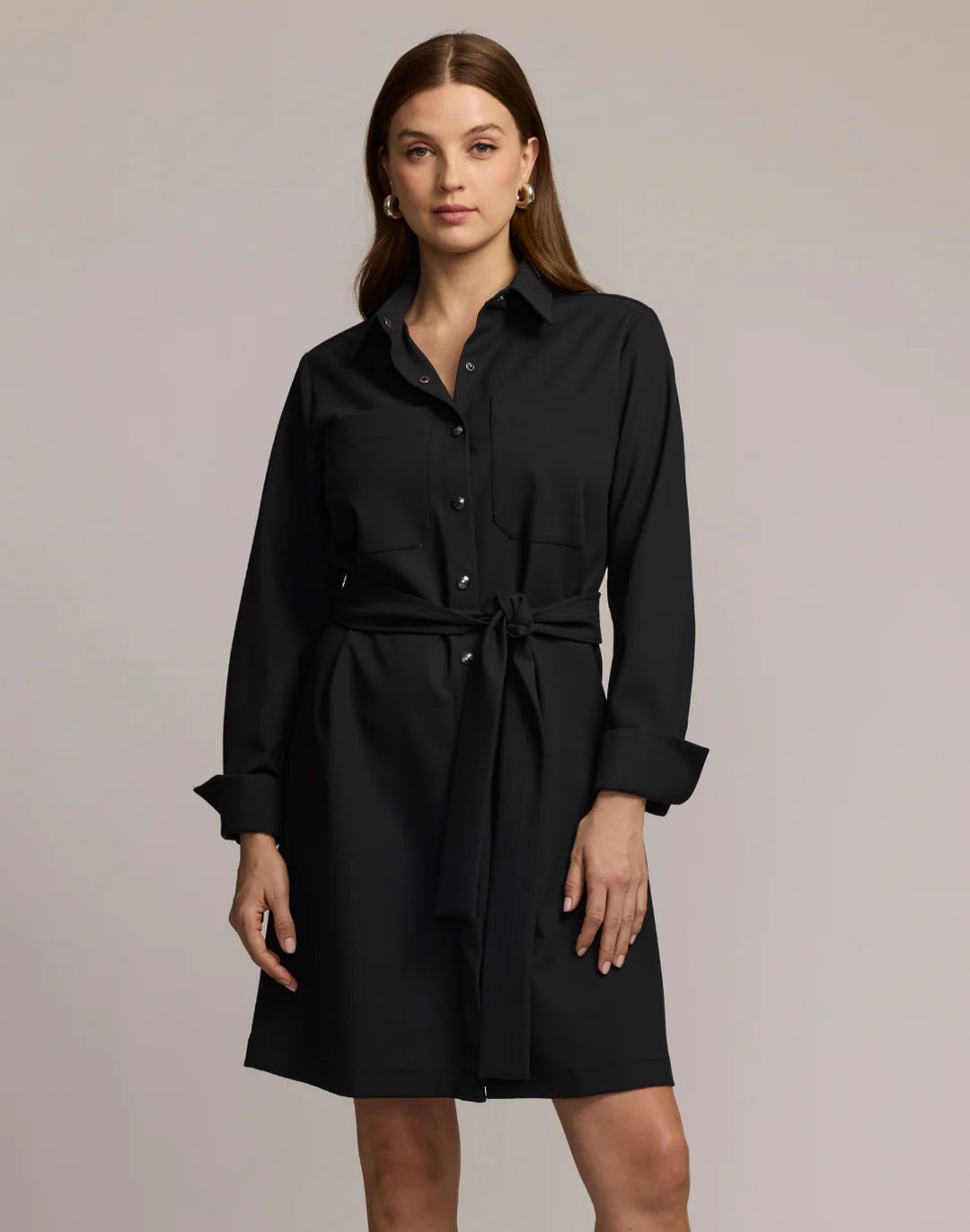 A woman with straight brown hair wears the HINSON WU Astrid Long Sleeve Traveler’s Twill Dress in black, featuring a collared neckline and tie waist, standing with her back to the camera against a neutral background.
