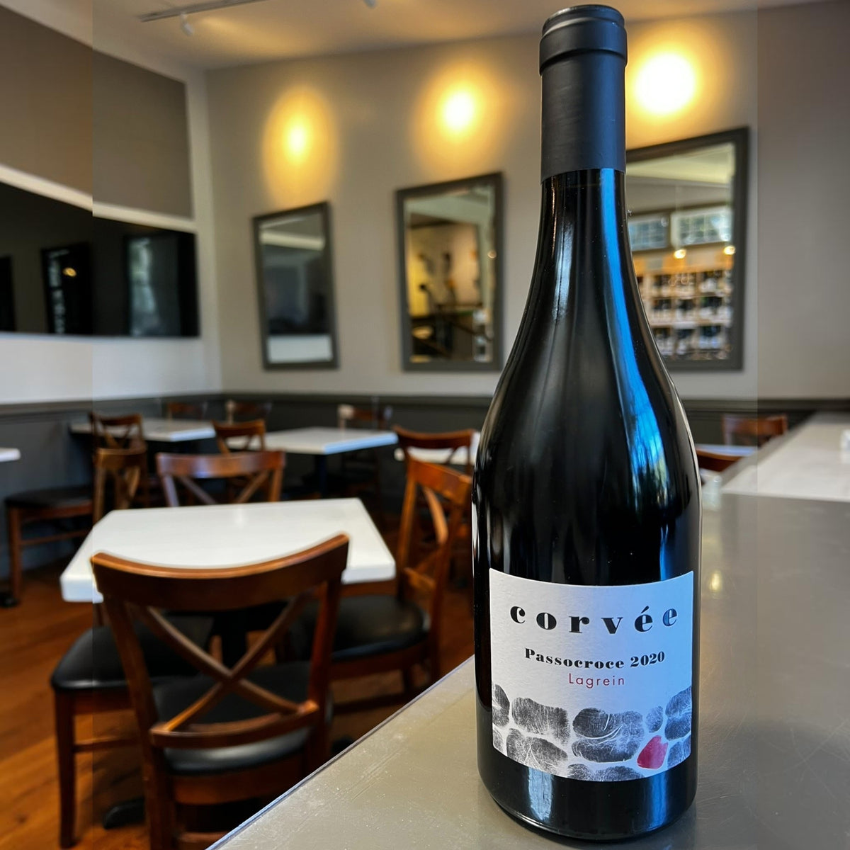 A dark wine bottle with a black cap. The white label reads “CORVEE PASSOCROCE LAGREIN 2020” and features a minimalist stone pattern with one stone colored red, reflecting the unique character of this mountain red wine from Val di Cembra, crafted by WINE: 3 KEYS.