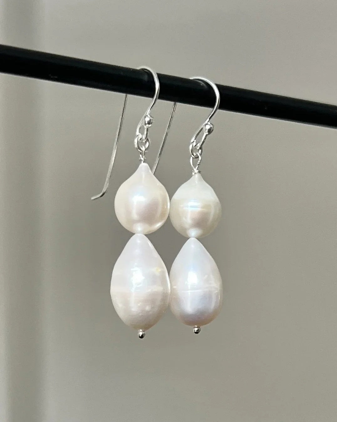 The ANN LIGHTFOOT - DOUBLE DROPLET FRESHWATER PEARL EARRINGS feature teardrop-shaped white pearls on sterling silver hooks, shown against a plain white background.