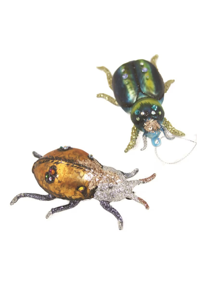 Two exquisite CODY FOSTER BEETLE ORNAMENT brooches, each measuring 4.25-4.5 inches in length, are displayed on a white background. The foreground beetle features a gold body with sparkling legs and red eyes, while the background beetle dazzles in green and blue with glittery details and silver legs.
