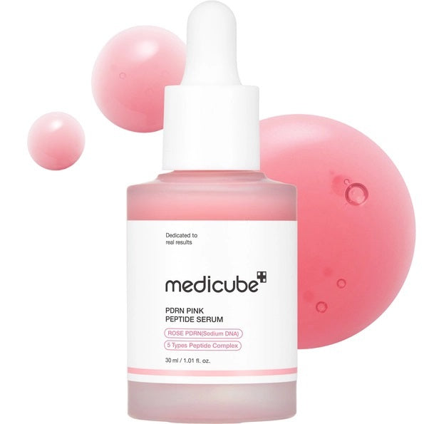 A pink dropper bottle of KOSMIC KBEAUTY SKINCARE MEDICUBE - PDRN PINK PEPTIDE SERUM, 30G is featured alongside large and small pink serum droplets in the background. The label emphasizes a peptide complex and PDRN/sodium DNA, making this glow serum an essential choice for a radiant complexion.