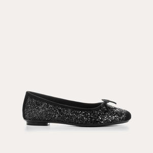 The REQINS Harmony Sequin Ballerina Flats in Noir feature black sequins, black toe caps, and small bows—bringing a touch of everyday luxury against a plain light background.