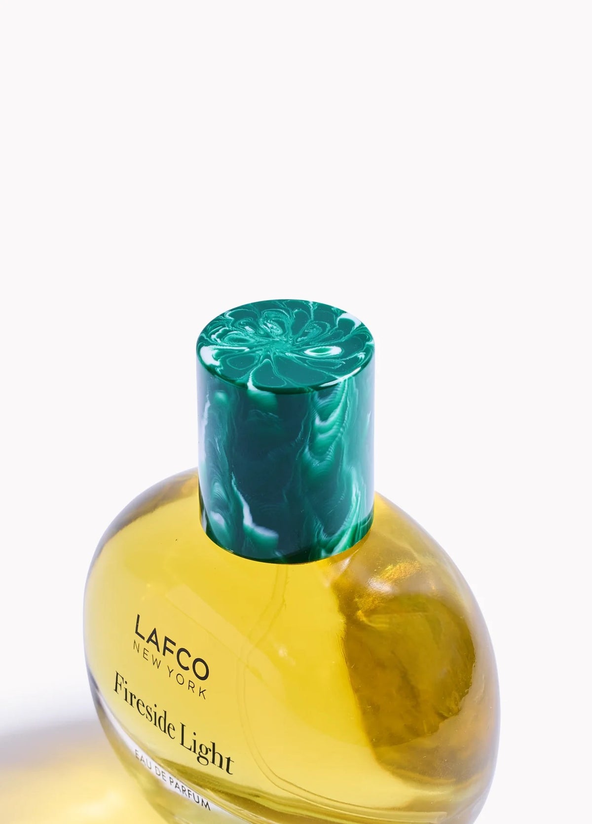 A round glass bottle of LAFCO Fine Fragrance, Fireside Light 50ml, a vegan perfume with a long-lasting scent, contains yellow liquid and is topped with a marbled green cap, displayed against a plain white background.