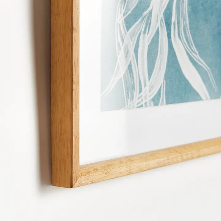 A framed protea abstract print in soft blue by NAPA HOME AND GARDEN, featuring a white floral illustration on a blue background. This botanical wall art is presented in a light wood frame for a fresh, contemporary look—perfect for modern home décor.