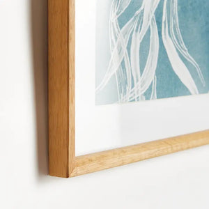 A framed protea abstract print in soft blue by NAPA HOME AND GARDEN, featuring a white floral illustration on a blue background. This botanical wall art is presented in a light wood frame for a fresh, contemporary look—perfect for modern home décor.