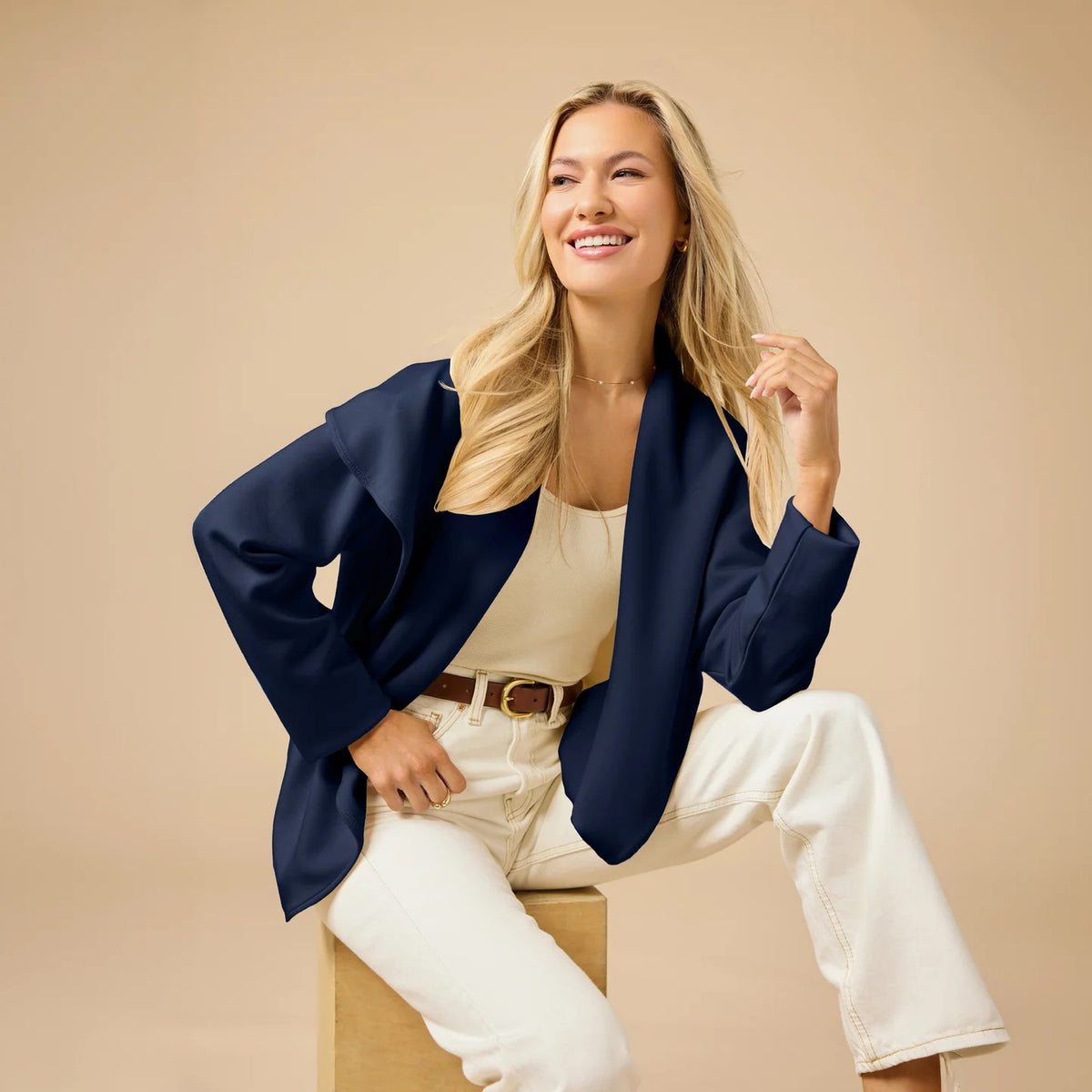 A woman wears an off-white SOFTIES - DREAMTECH EXAGGERATED COLLAR CARDIGAN with an exaggerated waterfall collar, cinched at the waist with a thin belt, and holds a matching handbag.