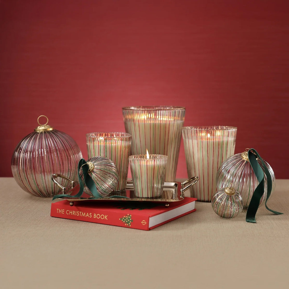 Ribbed, striped ALPINE STILL SCENTED CANDLE 6″ and ornaments arranged on a silver tray placed on a book titled The Christmas Book.