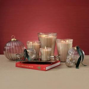 Ribbed, striped ALPINE STILL SCENTED CANDLE 6″ and ornaments arranged on a silver tray placed on a book titled The Christmas Book.